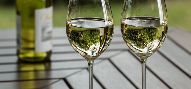 deux verres de vin posés sur une table avec une bouteille de vin blanc en arrière plan
