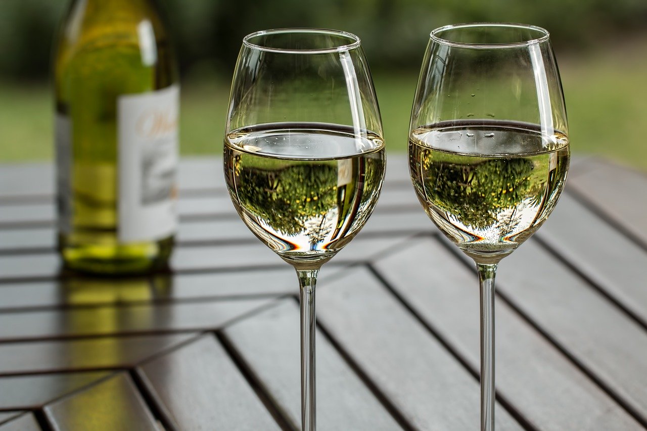 deux verres de vin posés sur une table avec une bouteille de vin blanc en arrière plan